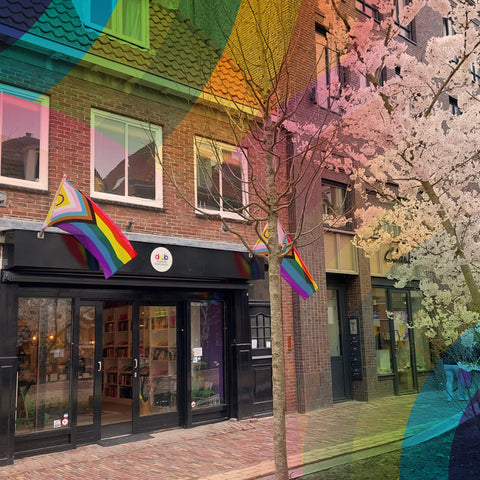 Shop front of De Queer Boekenkast, a warm and inviting bookstore with two rainbow progress flags outside