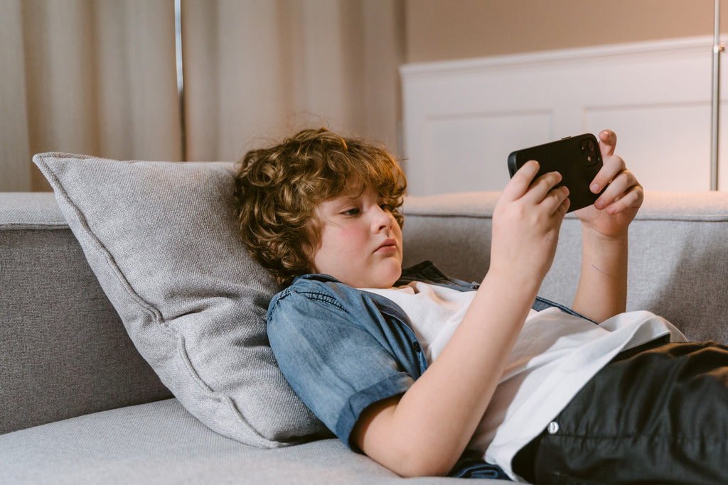 child lying on sofa with mobile phone