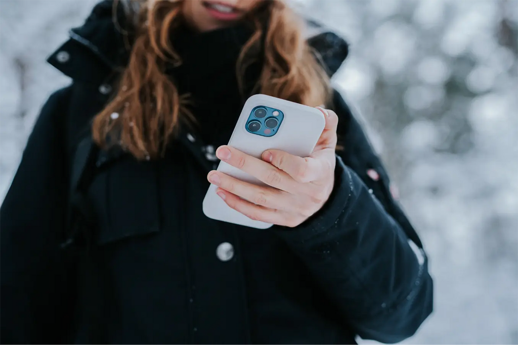 Kvinna i vinterjacka tittar på sin iPhone