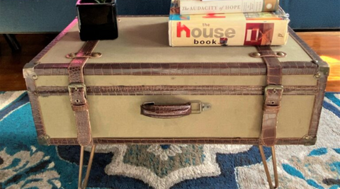 old suitcase with metal legs, standing on rug in living room, serving as a couch or side table