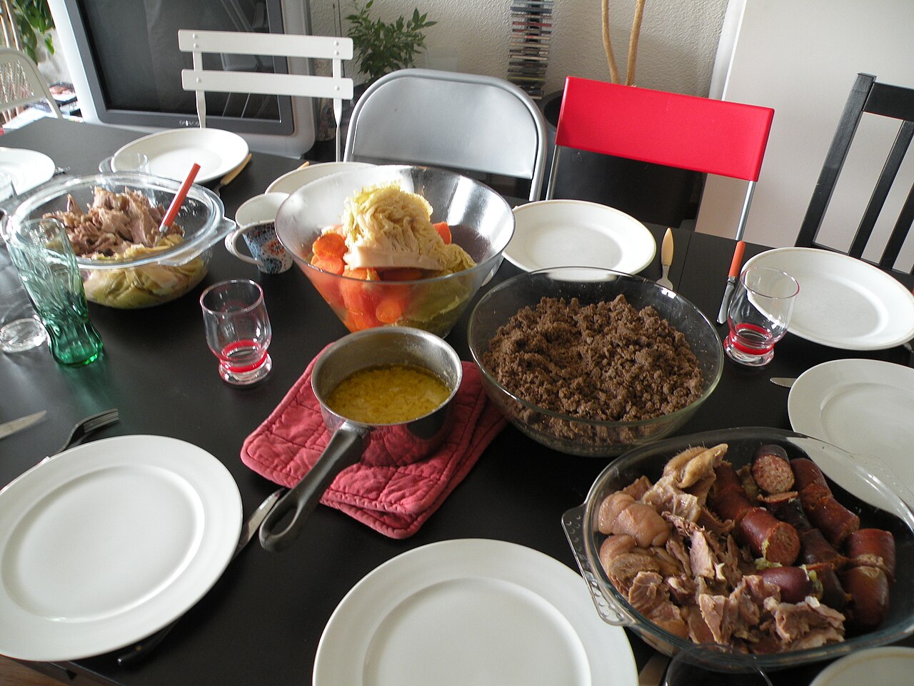 Table dressée pour un repas traditionnel breton, prête à servir le Kig ha farz, avec assiettes, couverts, et différents plats garnis de viandes, légumes, et farz émietté.