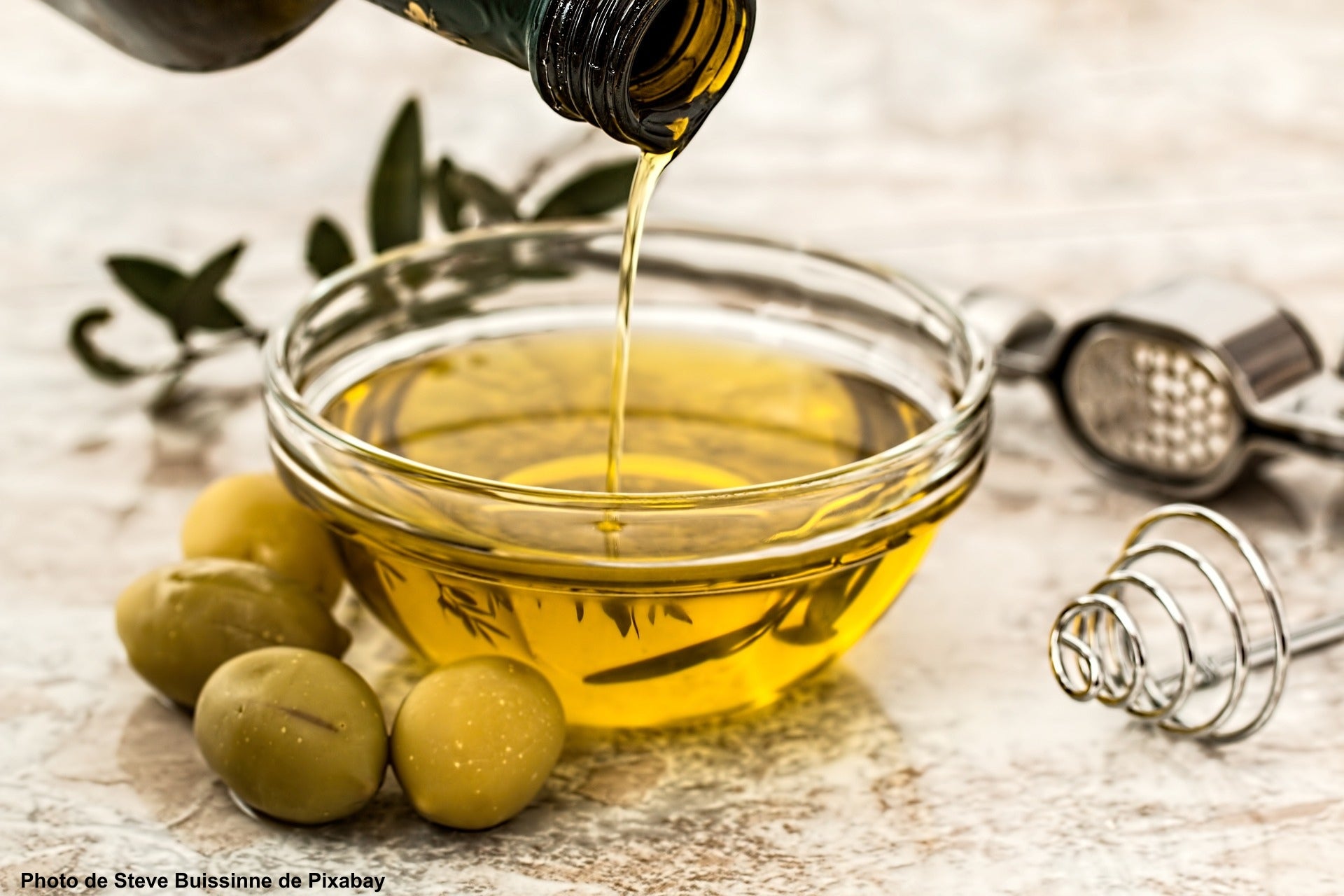 Huile d’olive coulant depuis une bouteille dans un bol posé sur une table avec des olives vertes et des ustensiles de cuisine – Photo de Steve Buissinne de Pixabay