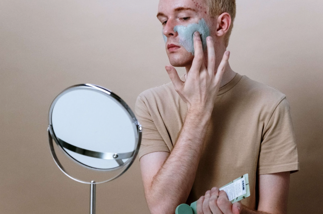 man applying skincare products in small mirror
