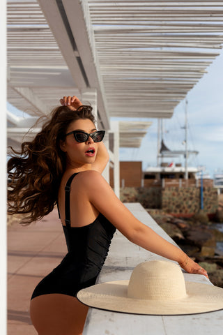 Elegant woman in Cannes wearing Sahra.Nko's black corset swimsuit, confidently posing on a pier with sunglasses and a straw hat