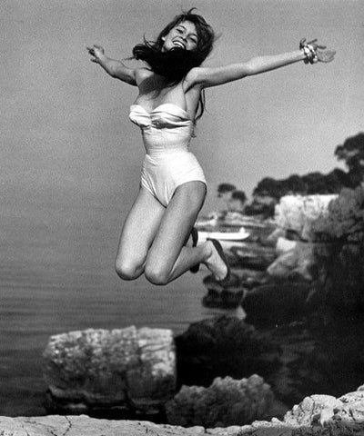 Joyful woman jumping on the beach in a vintage swimsuit, evoking classic style and carefree seaside holidays, inspired by Sophia Loren's timeless elegance.