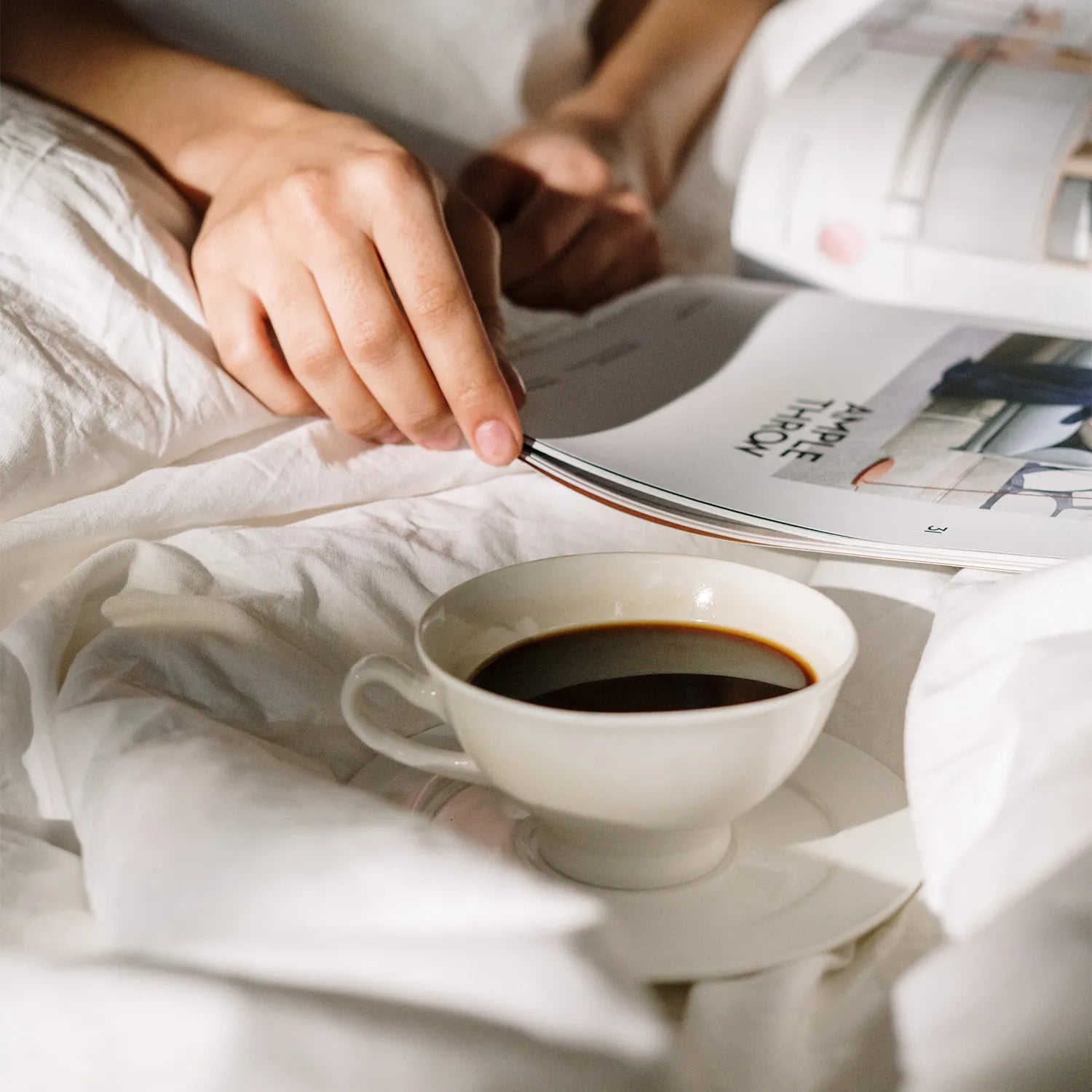Eine Frau liest im Bett bei einer Tasse Kaffee eine Zeitschrift, umgeben von natürlichen Elementen.