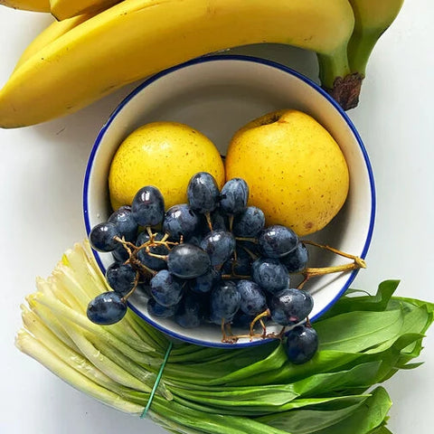 Eine Schüssel mit frischem Obst und Gemüse, darunter Bananen, Trauben, Äpfel und Blattgemüse