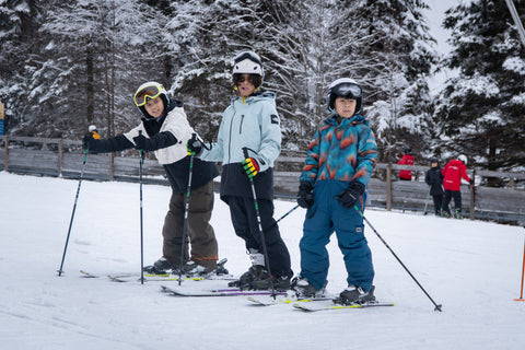 Three young kids standing in a row on skis