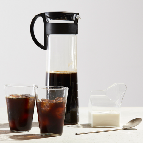 2 glasses of cold brew concentrate are placed in front of a Mizudashi brewer. A glass of milk and a spoon are off to the side.