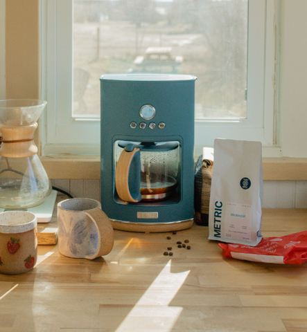 A blue coffee maker, two mugs, and a bag of coffee beans on a kitchen counter.