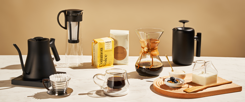 Various coffee-making equipment and a serving of coffee with light snacks on a countertop.