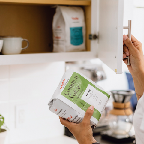 Person holding a bag of coffee while opening a kitchen cabinet.