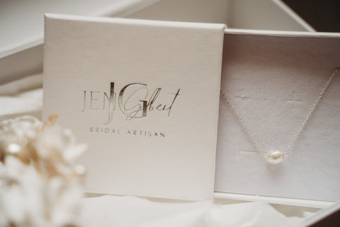 A single real pearl hung from a silver chain, nestled in a luxury white jewellery box