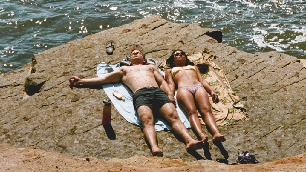 Couple qui bronze au soleil au bord de la mer allongés sur un rocher