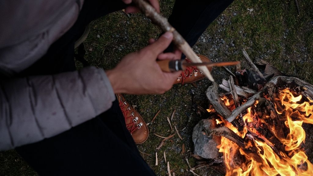 Bivouac et mains taillant un morceau de bois autour du feu de camp