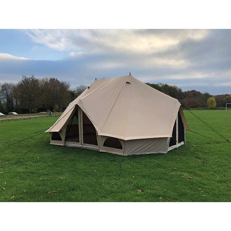 Spacious Emperor bell tent pitched on vibrant green grass under a moody sky, with scattered autumn trees in the distance.