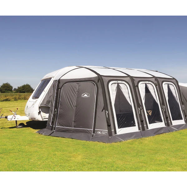 Grey and black air awning attached to a white caravan on a bright sunny day, set up on a green grassy field.