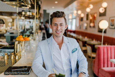 A smiling man in a light suit sitting at a modern, stylish bar or restaurant.