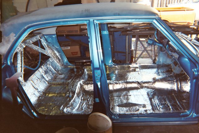 Muscle Car midst of a B-Quiet Sound Deadening upgrade. The vehicle's hood is open, exposing the engine bay prepared for soundproofing, while the interior is ready for the installation of B-Quiet's noise-reducing materials. The car is set against a backdrop of a busy garage, indicating an active sound deadening project. This setting exemplifies the practical application of B-Quiet's sound deadening solutions, designed for car enthusiasts looking to enhance their vehicle's acoustic comfort