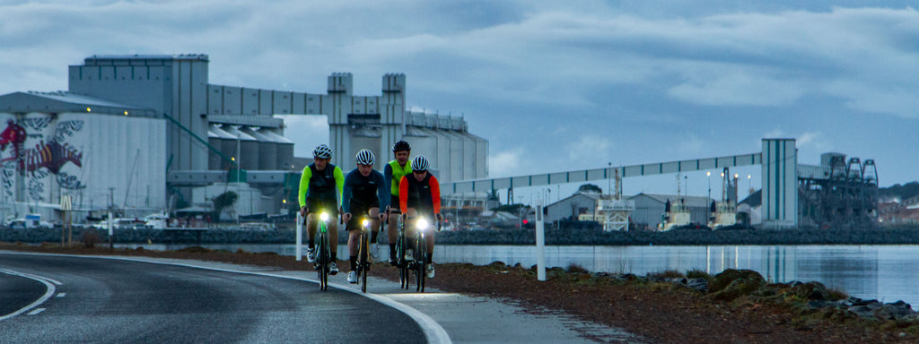 Riders riding in early morning low-light with lights and fluorescent elements to their clothing.