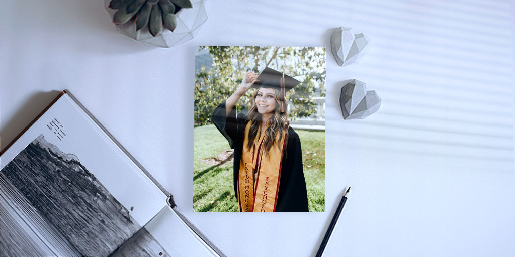 Custom photo print featuring a graduate in her cap and gown lay on a white desk.