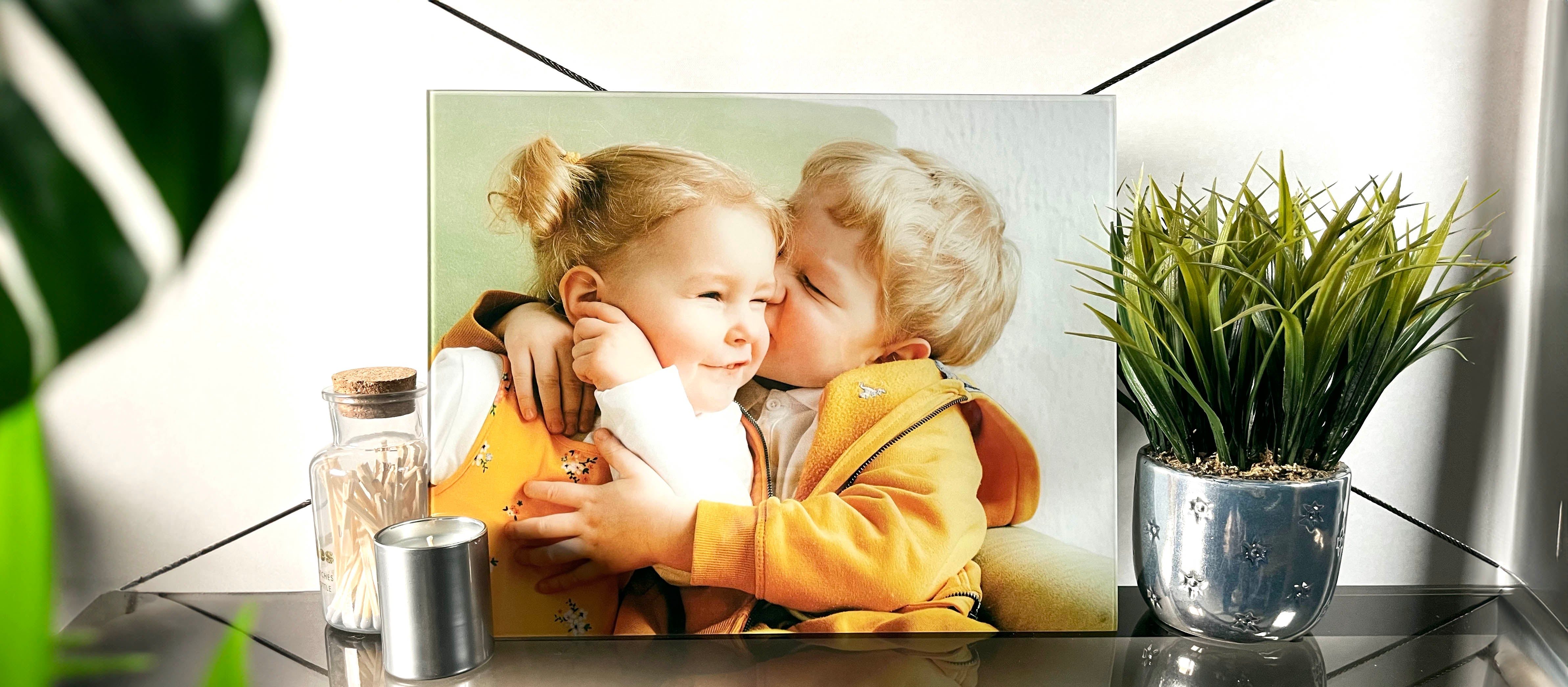 Custom photo print on glass featuring two young siblings, hugging and kissing sits on a glass table.