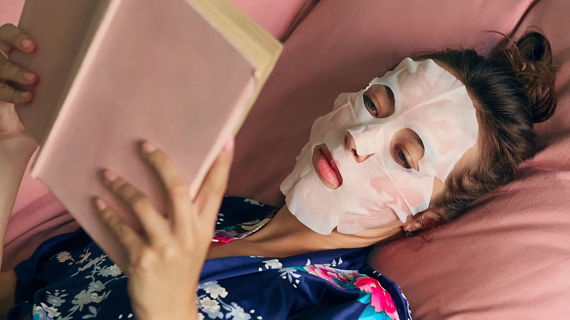 woman reading a book with a sheet mask on