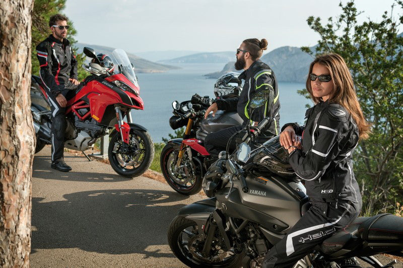 dwóch motocyklistów i jedna motocyklista przy motorach w widokiem na morze