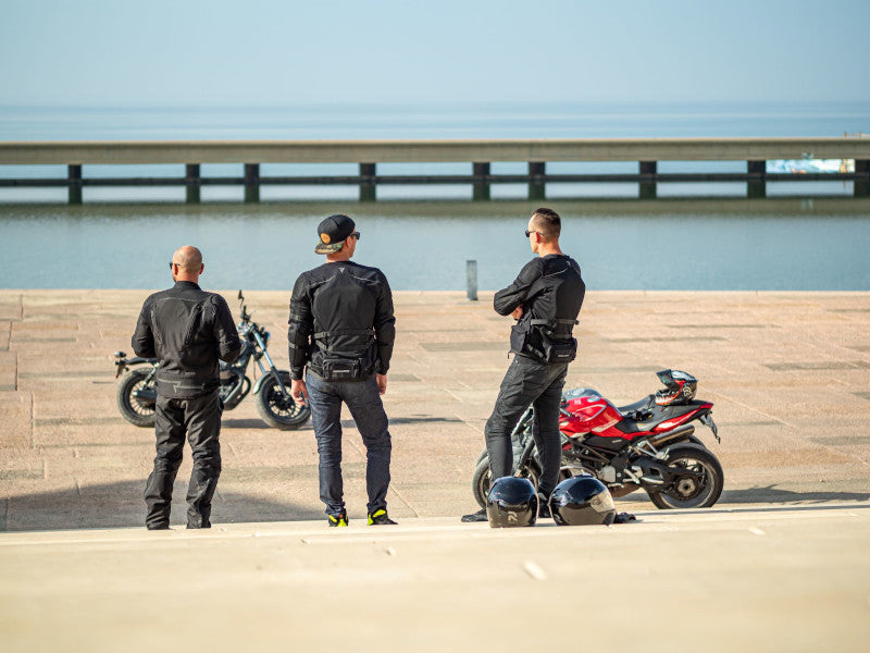 Three bikers stand on the beach wearing Rebelhorn Brutale clothes