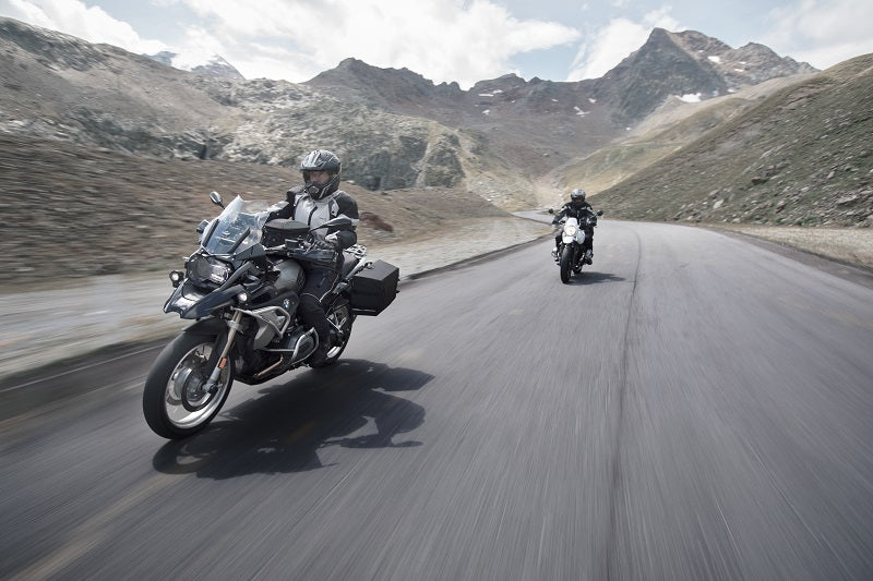 dwóch motocyklistów z sakwami na drodze jadą pomiędzy górami