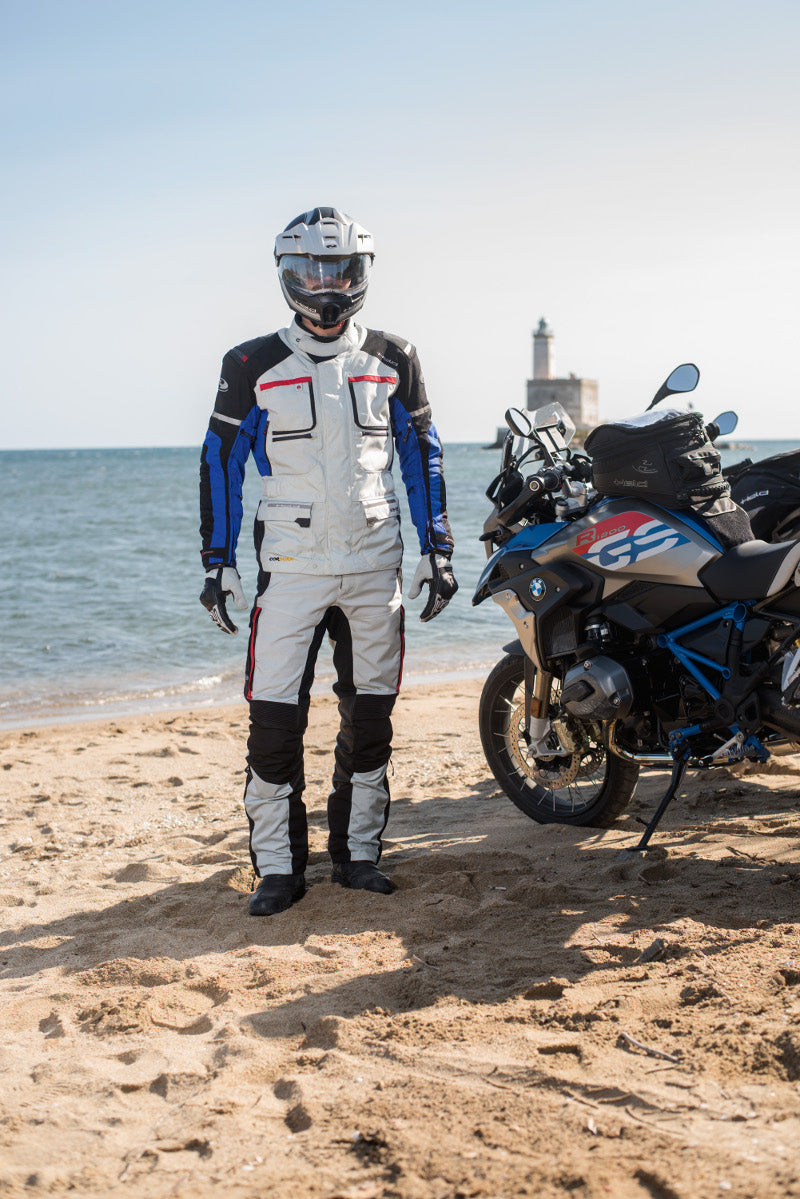 motocyklista w kurtce Carese II stoi na plaży obok motocykl BMW