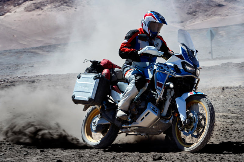 motocyklista na niebieskim motocyklu jedzie piaszczysta drogą
