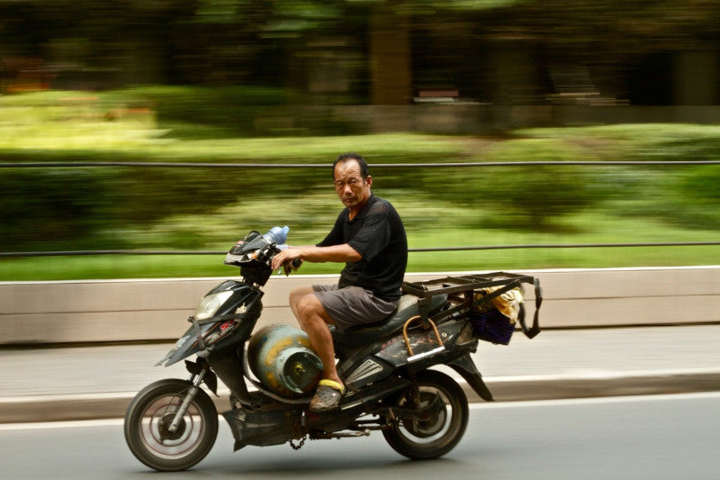 mężczyzna jedzie skuterem z butlą gazową pod nogami