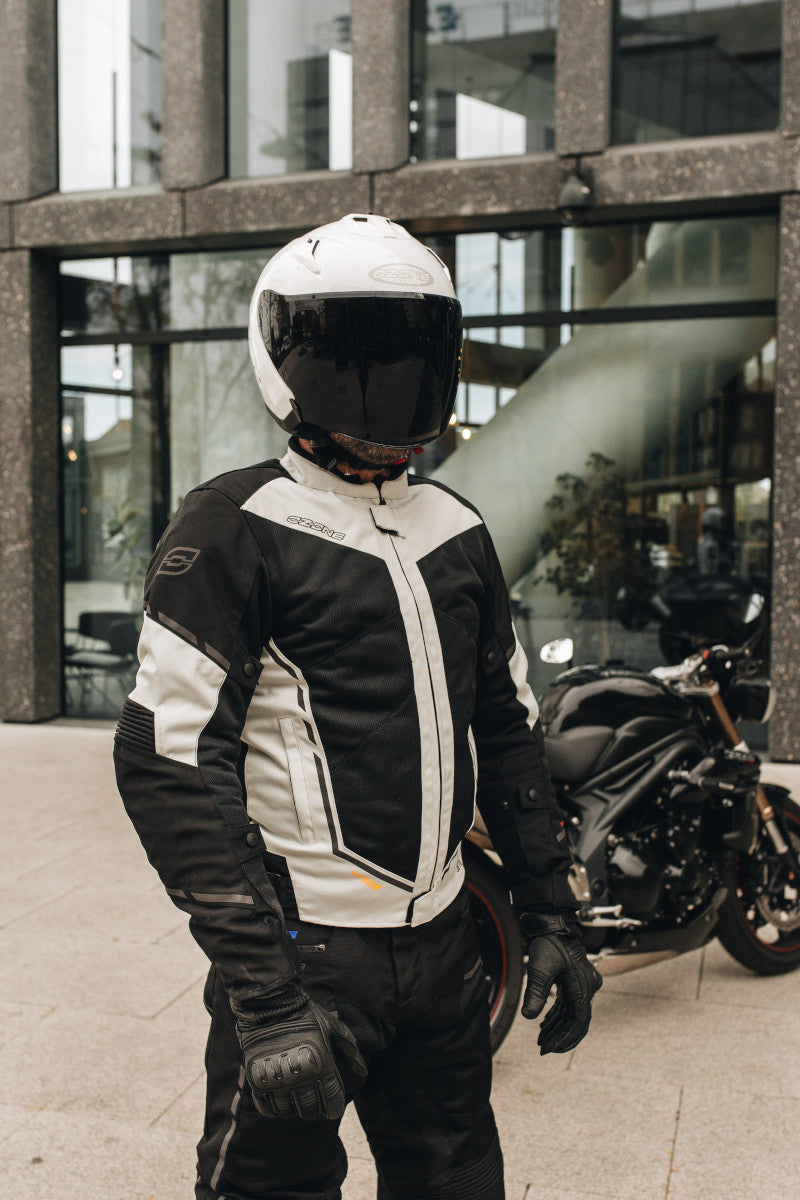 motocyklista stoi na chodniku, jest ubrany w białą kurtkę ozone jet ii