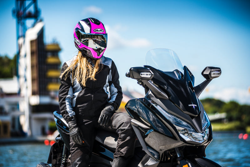 Motocyklista na motocyklu Honda ubrana w czarny kombinezon i różowy kask marki HJC