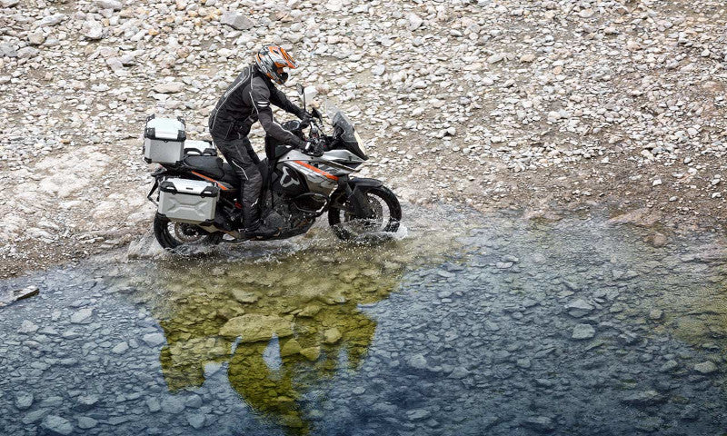motocyklista z kuframi na kamienistym brzegu przy jeziorze