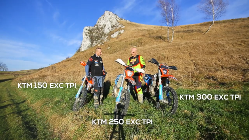 trzy motocykle i dwóch motocyklistów na zielonym pagórku. Napisy na fotografi KTM 150 EXC TPI, KTM 300EXC TPI, KTM 250 EXC TPI