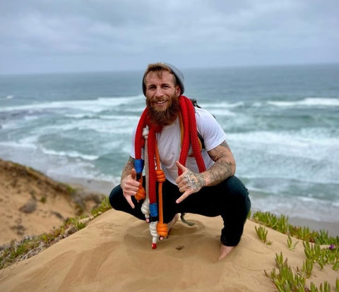 CJ Kobliska kneeling at the beach with ropes draped around his neck