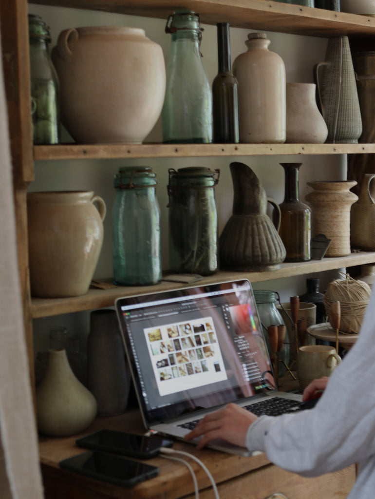 looking at images from shoot on laptop in a room surrounded by antique bottles and pots