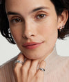 Woman wearing a white turtleneck and gold jewelry, highlighting a Round Gemstone Stacker Ring on her finger.