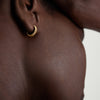 Close-up of a person's ear showcasing the Bold Micro Charlotte Huggie Hoop in Salmon Gold.