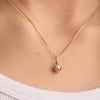 A person wearing a necklace featuring a blue sapphire Birthstone Sphere Charm pendant set in 14k solid gold.