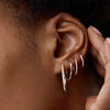 Close-up of a person wearing Pavé Diamond Small Hoops, handcrafted in recycled 14k solid gold, touching their ear.