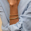 Person wearing a blue shirt showcasing the Bold Flexi Bangle on their wrist, featuring elegant gold design and craftsmanship.