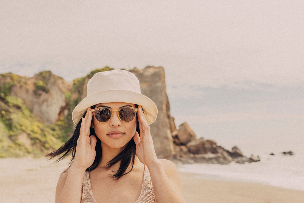 Woman on a sunny beach in a white hat touching her sunglasses
