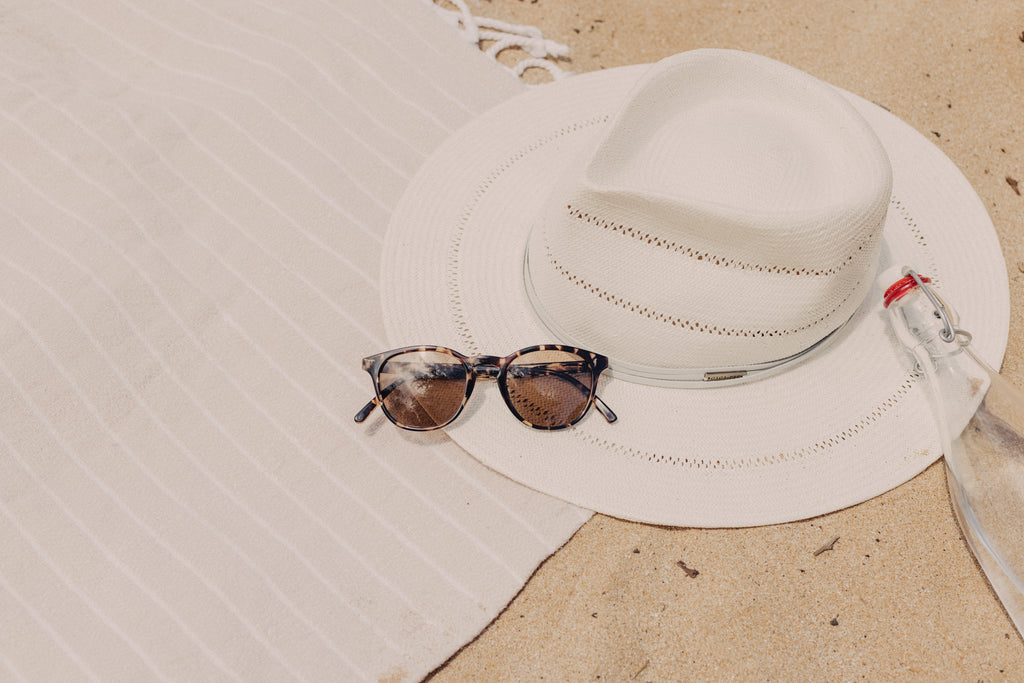 Sunglasses on a beach towel with water and a wide brim hat