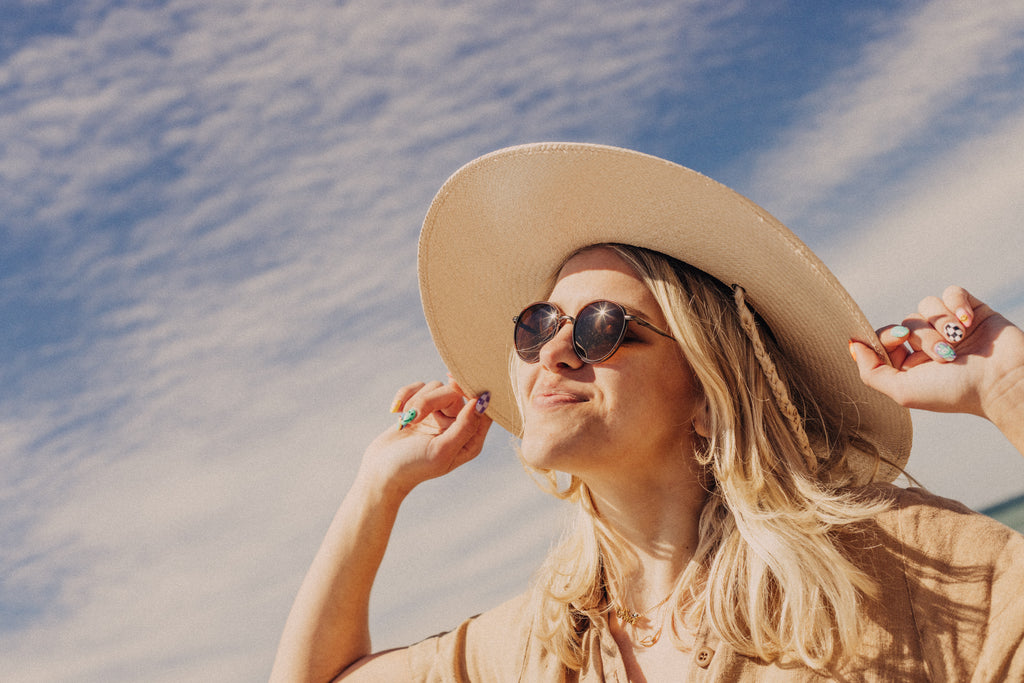 Woman in floppy white hat and sunglasses smiling in the sun