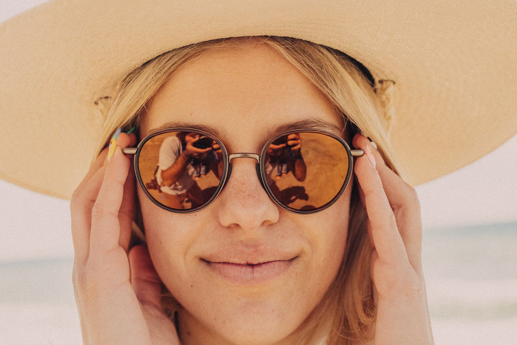 Close up of woman's face in sun hat and sunglasses on the beach