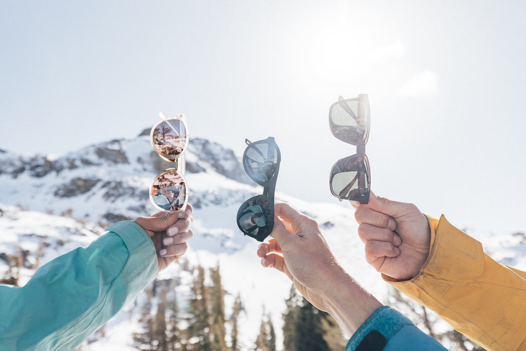 Three pairs of alpine sunglasses held up against a snowy mountain background