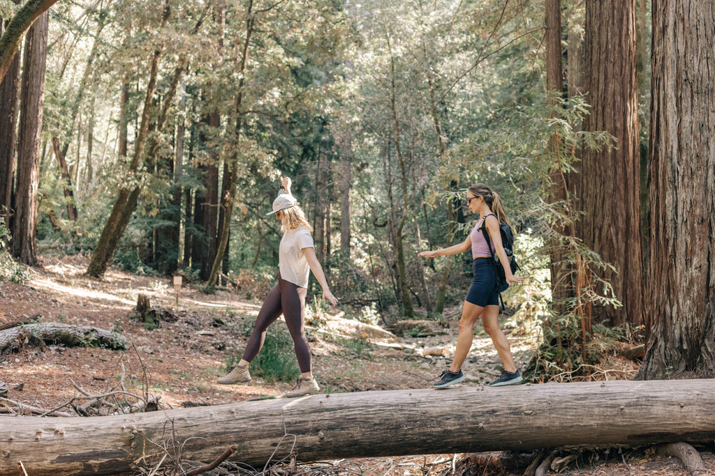 two women smiling as they walk across a log in the woods